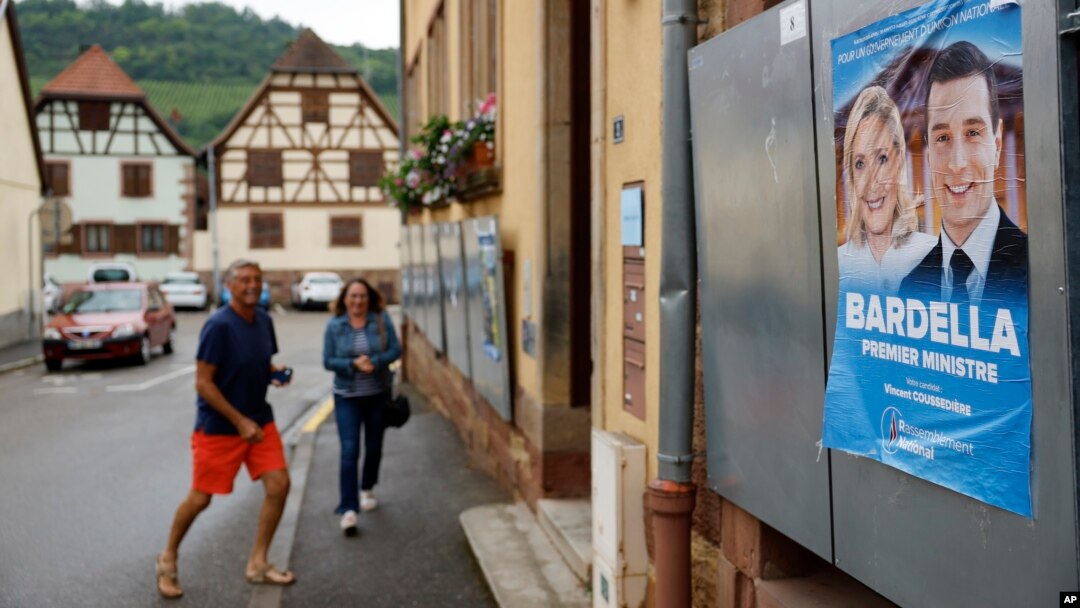 Voters arrive at a polling station in Soultz-Les-Bains, eastern France, June 30, 2024. A poster with French far-right leaders Marine Le Pen and Jordan Bardella is seen on the right.