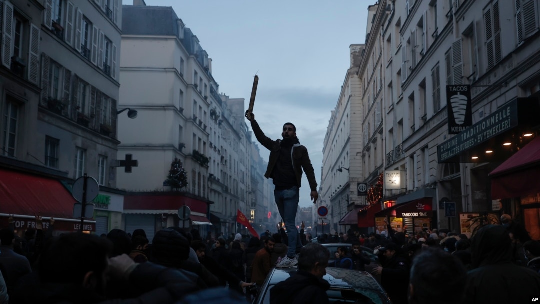 A member of the Kurdish community stands on the top of a car during clashes with police officers near the crime scene where a shooting took place in Paris, Dec. 23, 2022.