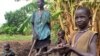 In this photo taken Tuesday, May 6, 2014 and made available Tuesday, May 13, 2014, John Kawai Lam, 8, right, plays with a non-functioning automatic rifle that he found buried in the soil when he and his mother Tabitha Nyanyun Ruach, 38, center, were culti