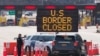 FILE - US Customs officers speaks with people in a car beside a sign saying that the US border is closed at the US/Canada border in Lansdowne, Ontario, on March 22, 2020.