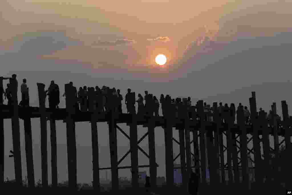 Local and foreign travelers stroll during the sunset along the U Bein Bridge, the longest wooden bridge that connect the two banks of Taungthaman Lake in Mandalay, central Myanmar, April 3, 2018.