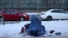 FILE - An Afghan woman holding her child begs on the snow-covered pavement in Kabul, Afghanistan, Jan. 27, 2022.