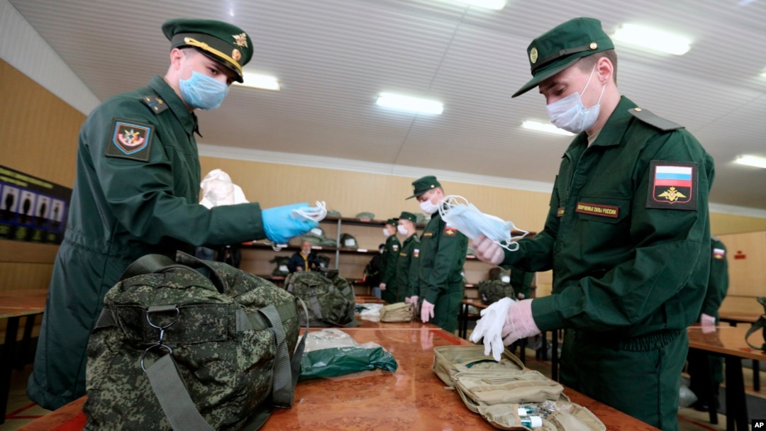 FILE - A Russian officer, left, hands face masks to a conscript at a military conscription office in Moscow, May 22, 2020. 