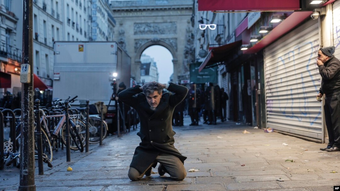 A member of Kurdish community kneels on the ground as he is detained during clashes stands with police officers near the crime scene where a shooting took place in Paris, Dec. 23, 2022.