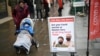 FILE - A woman, pushing a child in a stroller, walks past signage outside a pop-up vaccination site for COVID-19 vaccine and booster shots, in Hammersmith and Fulham, in Greater London, Britain, Dec. 3, 2021.
