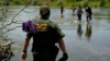 FILE - A Border Patrol agent watches as a group of migrants walk across the Rio Grande on their way to turn themselves in upon crossing the U.S.-Mexico border, June 15, 2021, in Del Rio, Texas.