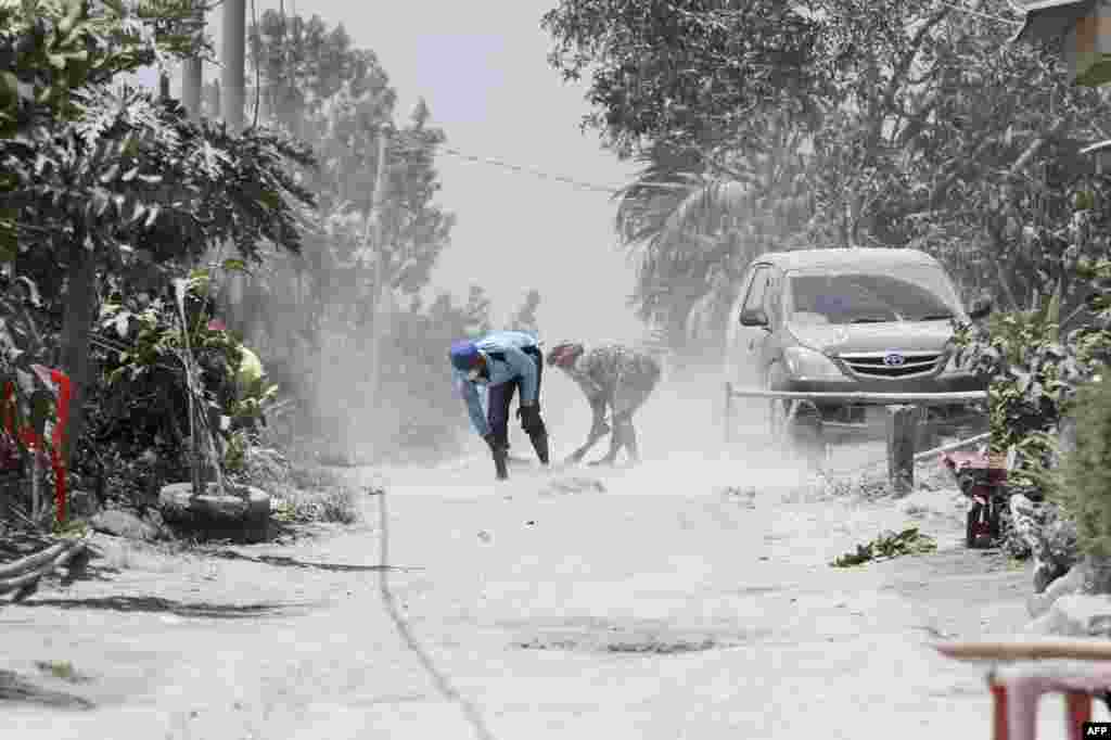 Men clean volcanic ash from the street after Mount Sinabung volcano spewed thick volcanic ash across the area the day before in Karo, North Sumatra, Indonesia.
