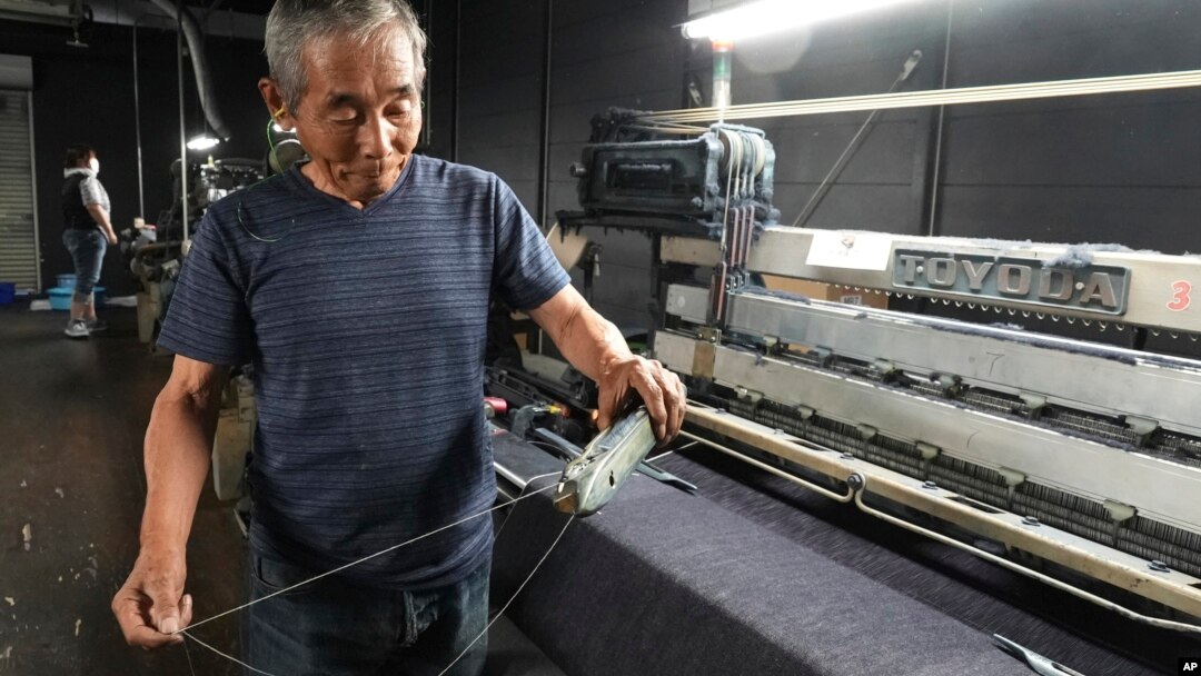 Shigeru Uchida, a weaver at Momotaro Jeans, holds a wooden shuttle next to a vintage loom machine in Kojima, Okayama prefecture, Japan, on Sept. 4, 2024. (AP Photo/Ayaka McGill)