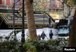 FILE - People walk past the screened-off facade of the Bataclan Cafe and its adjoining concert hall the day after a series of deadly attacks in Paris, Nov. 14, 2015.