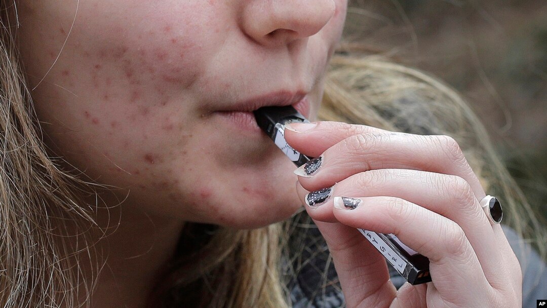FILE - A high school student uses a vaping device near a school campus in Cambridge, Massachusetts, April 11, 2018.