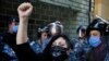 An anti-government protester wearing a mask to help curb the spread of the coronavirus with Arabic that reads, "Revolution," chants slogans while riot police stand guard in front of the Ministry of Economy, in downtown Beirut, Lebanon, May 11, 2020.