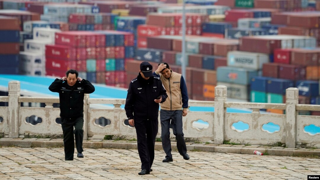 FILE - Security guards walk in front of containers at the Yangshan Deep Water Port in Shanghai, China, April 24, 2018.