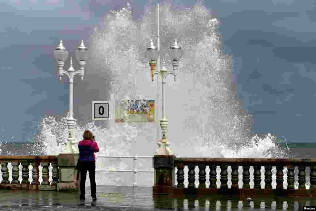 A woman takes pictures of a huge wave crashing against the promenade at San Lorenzo beach in Gijon, Spain.