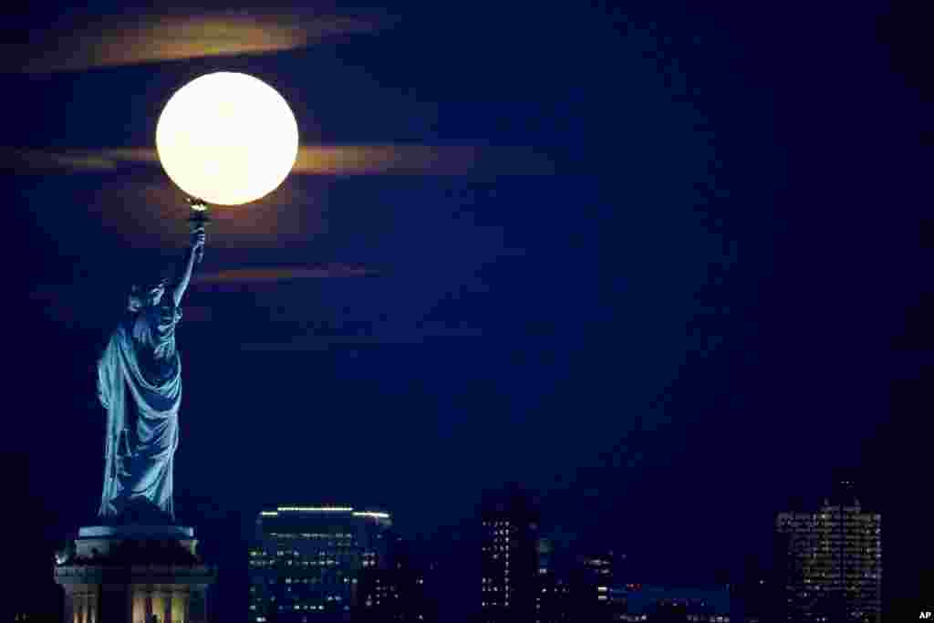 A full moon rises over the Statue of Liberty, seen from the Port Liberte neighborhood of Jersey City, New Jersey, Feb. 22, 2016.