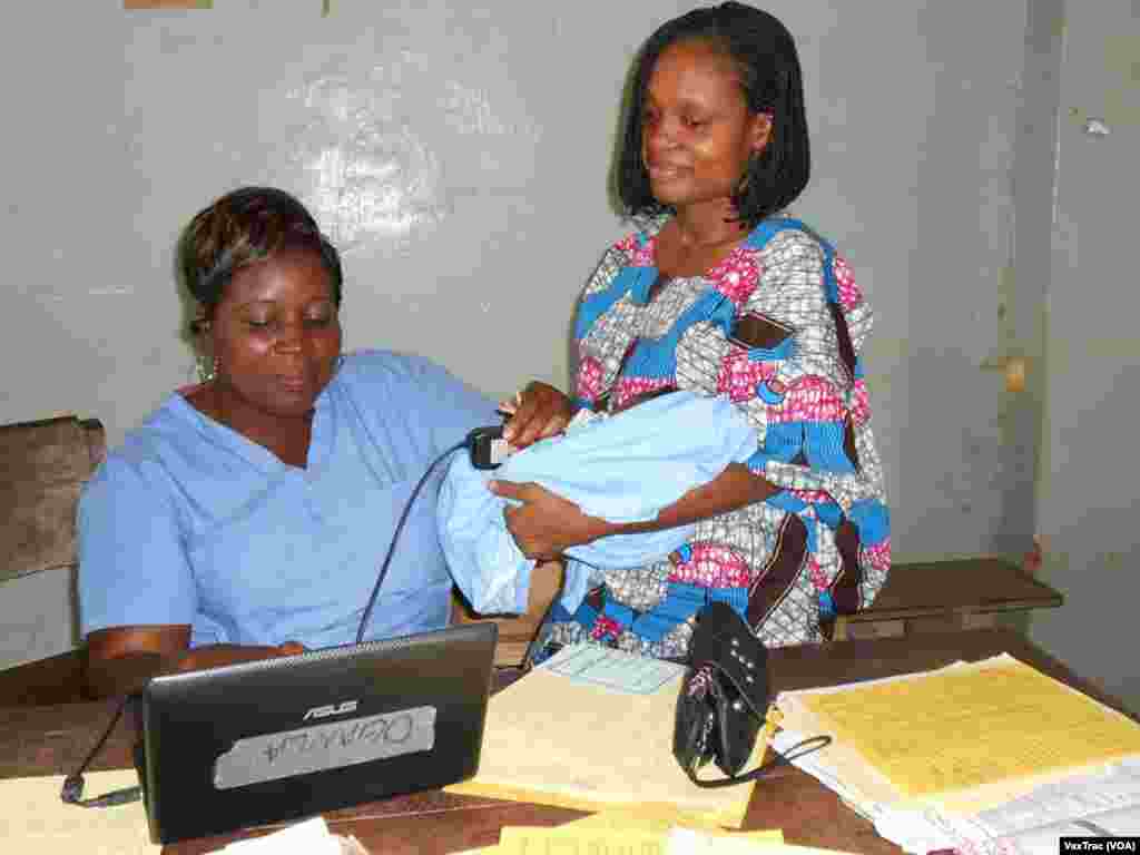 A health care worker holds a baby’s finger on a scanning device to capture its fingerprint at a clinic in Benin. (VaxTrac)
