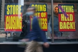 FILE - People walk past a business that is closing following the outbreak of COVID-19 in the Manhattan borough, New York, Aug. 17, 2020.