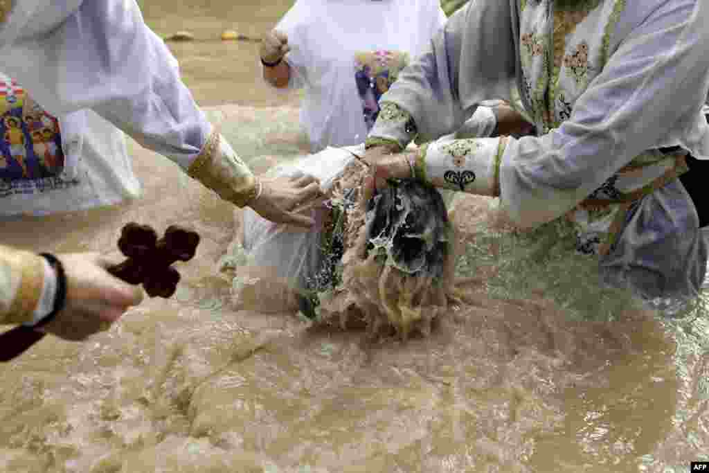 A Romanian Christian Orthodox priest baptizes a pilgrim in the muddy water of the Jordan River during the Epiphany celebrations at the Qasr al-Yahud baptismal site near the West Bank city of Jericho.