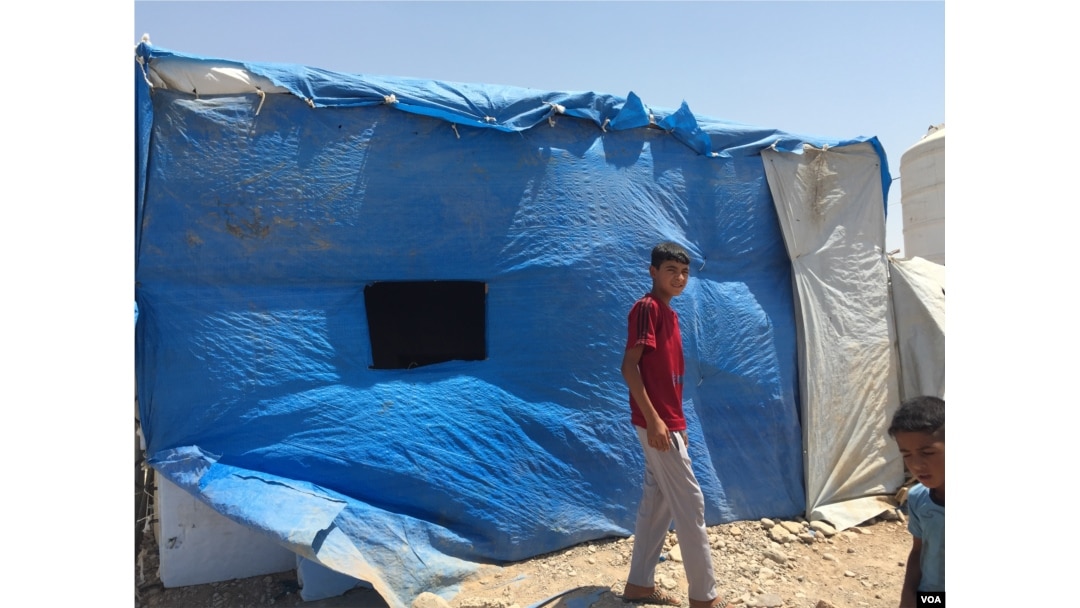 A displaced Sunni teenager walks past a blue plastic covered building in Baharka camp which houses just under 4,000 people on the outskirts of Irbil, in the Kurdistan region of Iraq, Aug, 2015. (VOA / S. Behn)