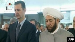 An image grab taken from the state-run Syrian television on August 8, 2013, shows Syrian President Bashar al-Assad (L) and Syrian Grand Mufti Ahmed Hassun attending the morning prayer of Eid al-Fitr in Damascus.