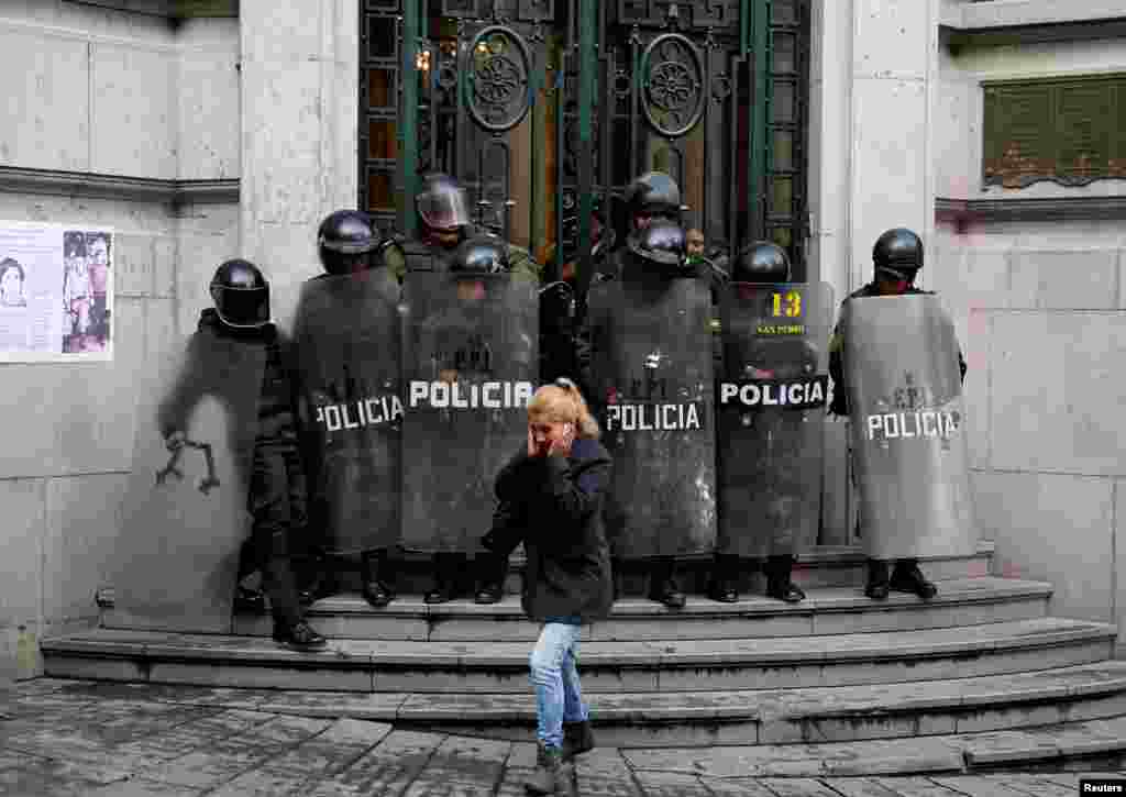 A pedestrian walks in front of riot policemen at the Bolivian Vice Presidency during a rally protest against Bolivia's government new health care policies in La Paz, Jan. 8, 2018.