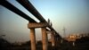 FILE - Men carry jerry cans as they walk along a pipeline in Karachi, Pakistan, on May 2014.