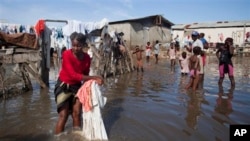 Bernard Sylphanie cleans her belongings in floodwater outside her home in Cap-Haitien, Haiti, Friday, Nov. 7, 2014. Thousands of families in Haiti and the neighboring Dominican Republic have been affected by floods from a storm system that drenched the countries for several days. At least five people were killed and one was missing. Floods raise the risk of cholera and dysentery outbreaks. (AP Photo/Dieu Nalio Chery)