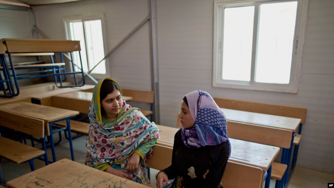 FILE - Nobel Peace Prize laureate Malala Yousafzai, 18, left, and Mezon al-Melihan, a 17-year-old refugee from the southern Syrian town of Deraa, talk while visiting a class at Azraq refugee camp, Jordan, July 13, 2015.