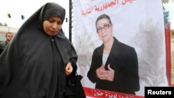 FILE - A women walks past electoral posters of Louisa Hanoune, a candidate for Algeria's Workers' Party in the 2014 presidential election, March 27, 2014.