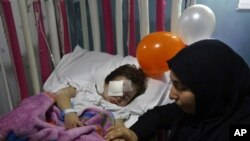 Adraa Taleb holds the hand of her maternal cousin Haidar Mustafa, three, who was wounded in Thursday's twin suicide bombings, as he sleeps on a bed at the Rasoul Aazam Hospital in Burj al-Barajneh, southern Beirut, Lebanon, Friday, Nov. 13, 2015.