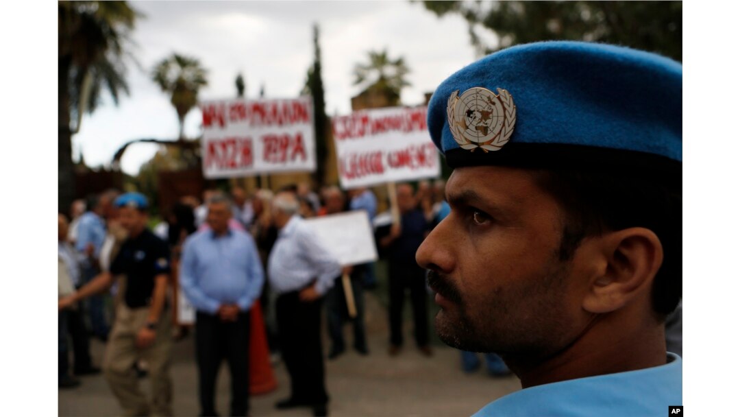 FILE - A U.N. peacekeeper stands guard in front of Greek and Turkish Cypriots as they gather outside the Ledra Palace Hotel, Nicosia, Cyprus, May 11, 2015.