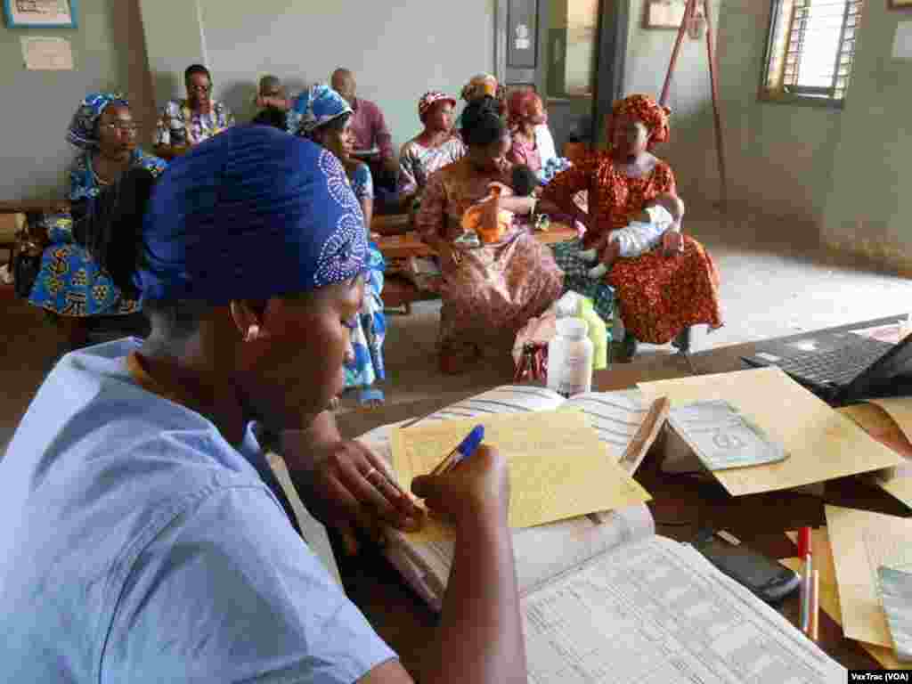 A health care worker fills out an immunization record by hand as mothers wait for vaccinations at a clinic in Benin. (VaxTrac)