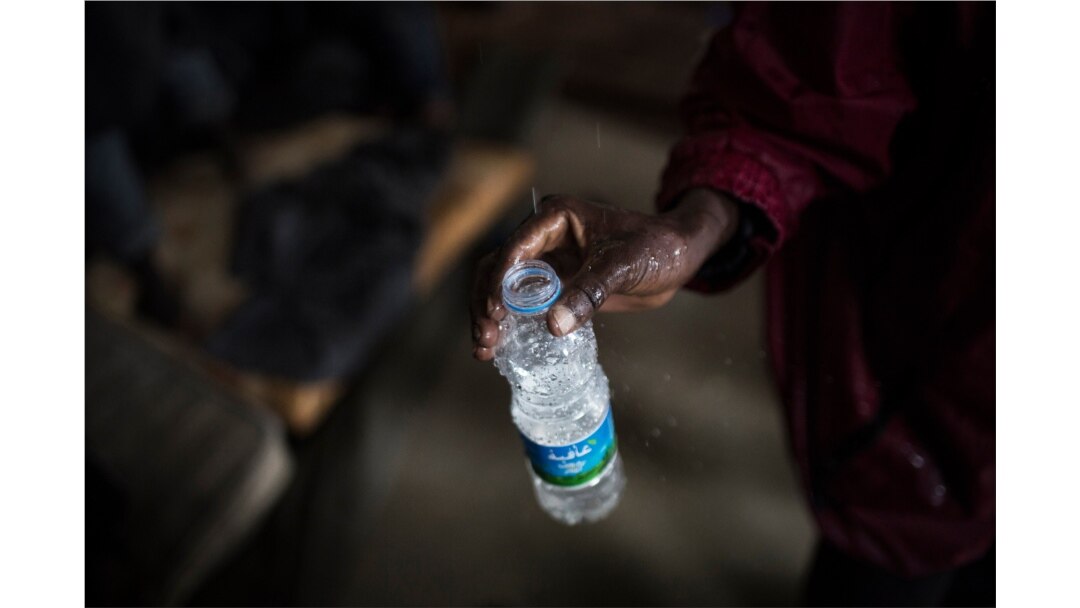 FILE - An African migrant fills an empty bottle with leaking water from the roof of a barrack in a detention center for illegal migrants in Abu Salim district on the outskirts of Tripoli, LIbya, Nov. 29, 2013.