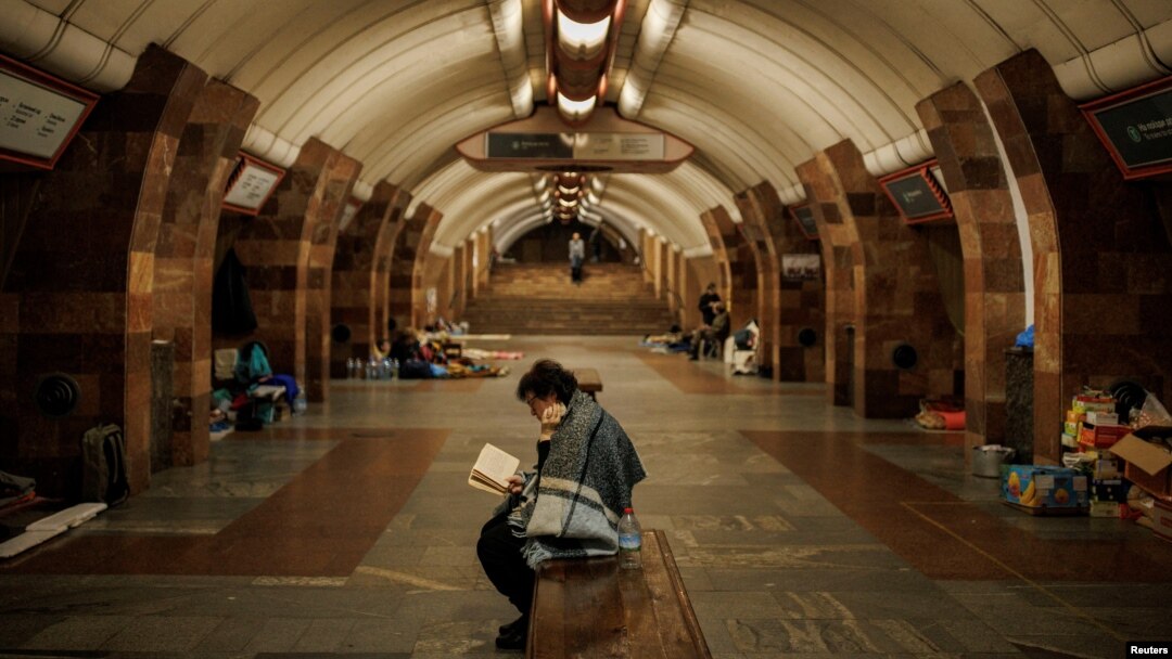 สตรีชาวยูเครนนั่งอ่านหนังสือในสถานีรถไฟใต้ดินที่เมืองคาร์คิฟ ซึ่งถูกใช้เป็นสถานที่หลบภัยการโจมตีของรัสเซีย