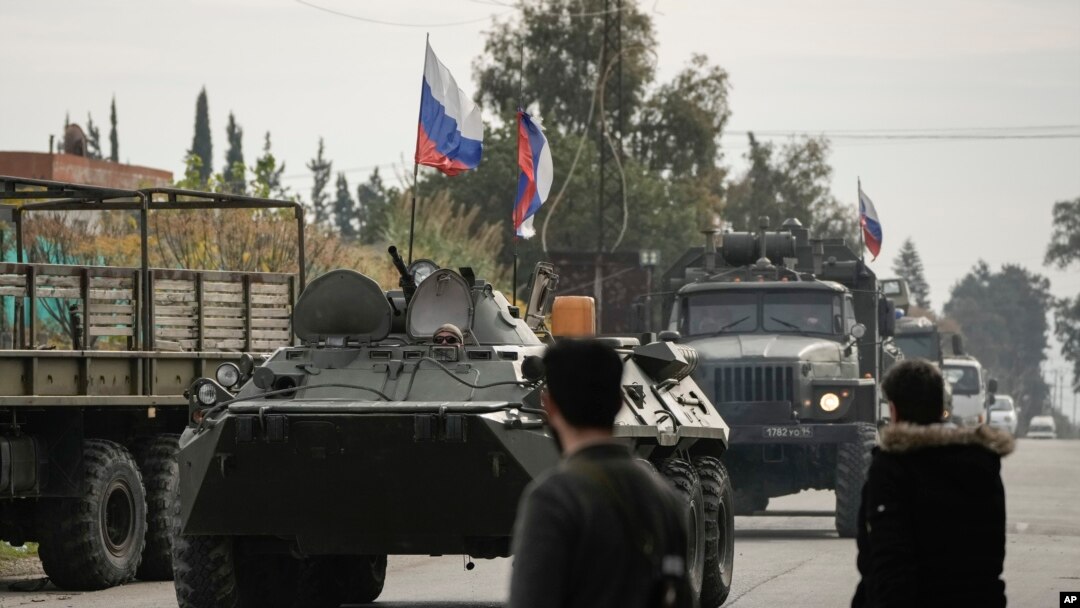 ARCHIVO - Combatientes sirios observan vehículos blindados rusos pasar cerca de la base aérea de Hmeimim, una base aérea siria actualmente operada por Rusia, en la ciudad de Hmeimim, al sureste de Latakia, Siria, el lunes 16 de diciembre de 2024. AP