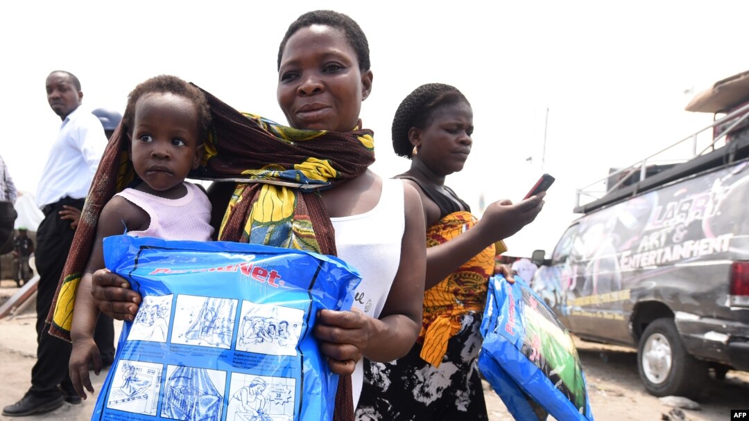 A woman carrying a baby holds a treated mosquito net during a malaria prevention action at Ajah in Eti Osa East district of Lagos, Nigeria, April 21, 2016.
