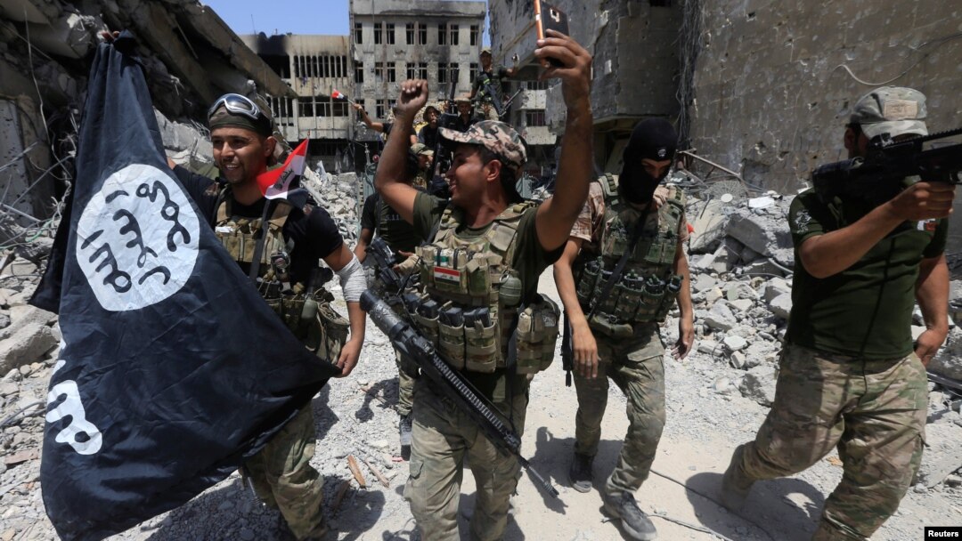 FILE - Members of Iraq's Emergency Response Division hold an Islamic State flag that they pulled down as they celebrate in the Old City of Mosul, Iraq, July 8, 2017. Islamic State fighters have mostly been pushed out of Iraq and Syria but are far from defeated.