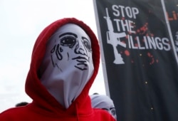 FILE - A masked protester stands next to a banner condemning President Rodrigo Duterte's war on drugs, during a rally to coincide with his third State of the Nation Address, July 23, 2018, in Quezon city, metropolitan Manila, Philippines.