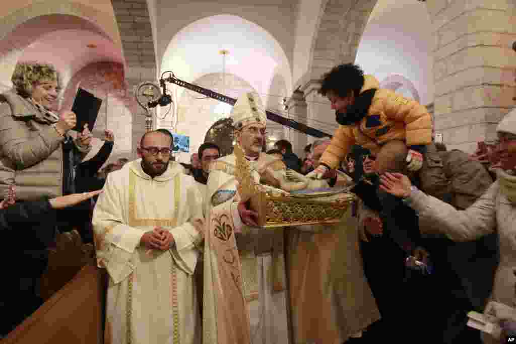 Archbishop Pierbattista Pizzaballa, center, apostolic administrator of the Latin Patriarch of Jerusalem, holds a statue of Baby Jesus in Saint Catherine's Church at the end of the Christmas Midnight Mass and walks in procession to the 'Grotto', where Christians believe the Virgin Mary gave birth to Jesus Christ, in the adjacent Church of the Nativity in Bethlehem, West Bank, Dec. 25, 2016.