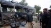 Security officials stand near a damaged police bus at the site of an explosion in Karachi, Feb. 13, 2014. 