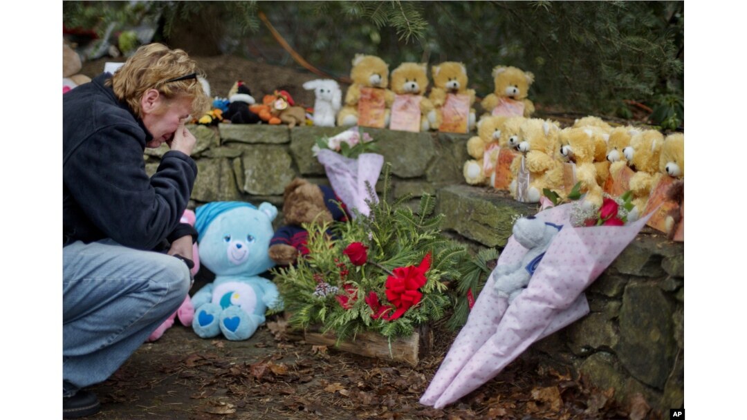 FILE - Cheryl Girardi, of Middletown, Conn., kneels beside 26 teddy bears, each representing a victim of the Sandy Hook Elementary School shooting, at a sidewalk memorial, Dec. 16, 2012, in Newtown, Conn.