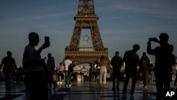 Люди зі смартфонами на тлі Ейфелевої вежі в Парижі, 7 червня 2024. AP Photo/Aurelien Morissard