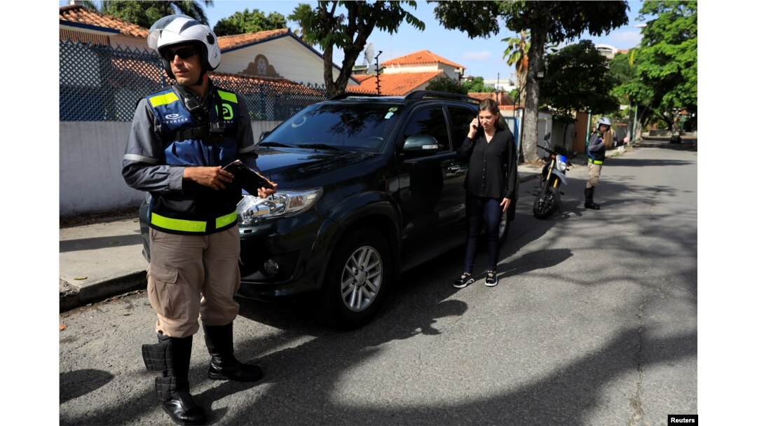 Vanessa Mikuski makes a phone call as employees of Pana, a mobile application which dispatches security crews to stranded drivers who request help, stand guard next to her in Caracas, Venezuela, June 15, 2018.