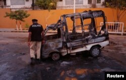 A policeman inspects a vehicle burned by Mutahida Qaumi Movement (MQM) political party protesters, in Karachi, Pakistan, Aug. 22, 2016.