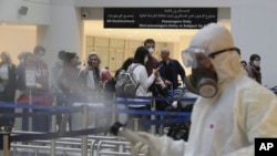 FILE - Passengers line up as workers wearing protective gear spray disinfectant as a precaution against the coronavirus outbreak, in the departure terminal at the Rafik Hariri International Airport, in Beirut, Lebanon, March 5, 2020.