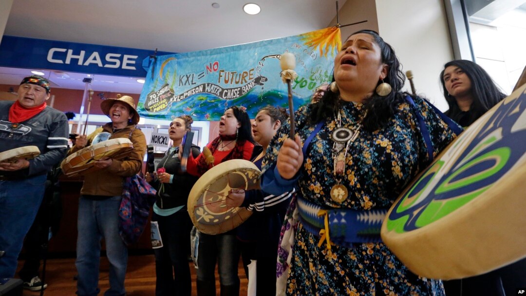 FILE - Roxanne White, right, a member of the Yakama Nation, sings during a protest inside a Chase bank branch, May 8, 2017, in Seattle. Climate activists opposed to oil pipeline projects have called on several financial institutions not to help build pipelines.