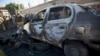 A policeman, background, takes a picture of a damaged car with his cellphone at the scene of a car bombing outside a police academy in Sana'a, Yemen, Jan. 7, 2015. 