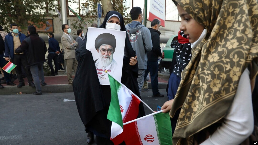 FILE - A demonstrator holds a portrait of the Iranian Supreme Leader Ayatollah Ali Khamenei as a girl holds the country's national flag in a rally in front of the former U.S. Embassy commemorating the anniversary of its 1979 seizure in Tehran, Iran, Nov. 