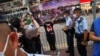 香港警察在维多利亚公园外拦截一名妇女，她身穿纪念六四的T恤，做出反送中运动“五大诉求 缺一不可”的手势。（2021年6月4日）