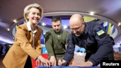 Президент України Зеленський, прем'єр-міністр Шмигаль і президентка Єврокомісії фон дер Ляєн підписують державний прапор України перед початком саміту ЄС у Києві.