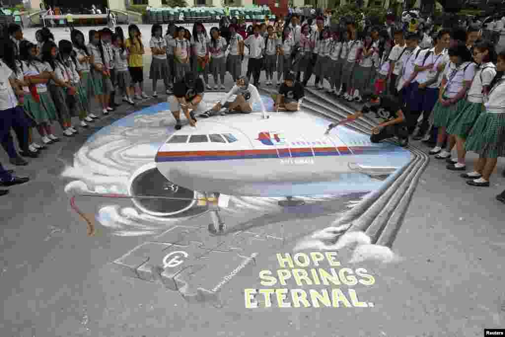 Students watch as a group of artists finish a piece based on the missing Malaysia Airlines flight MH370 that was painted on a school ground in Makati city, metro Manila, Philippines, March 17, 2014.